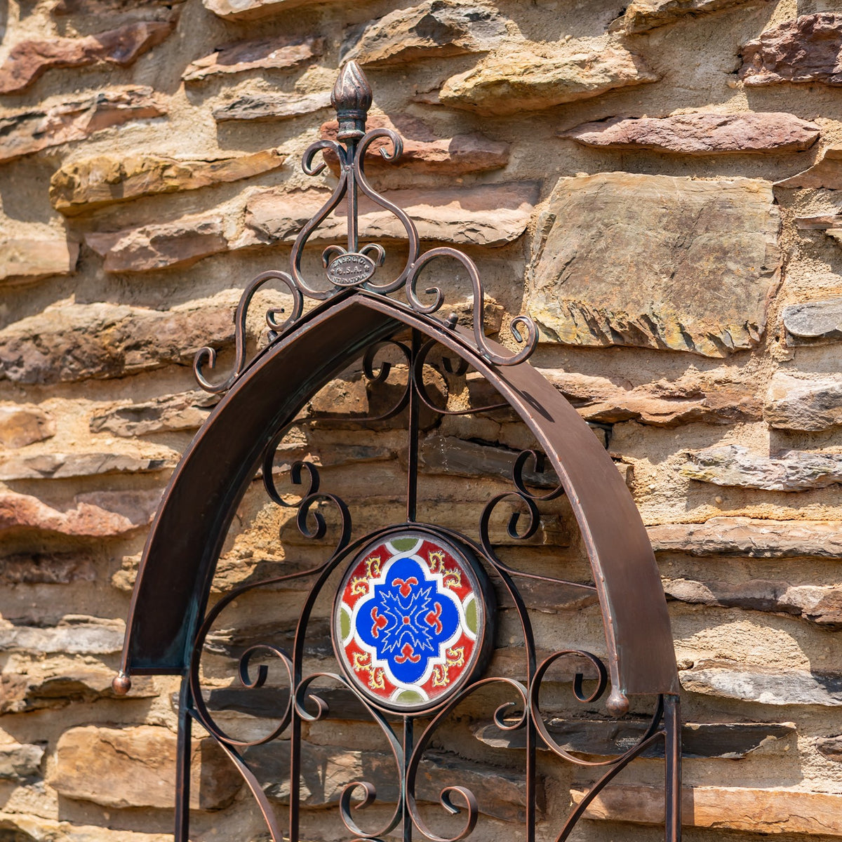Ornate bronze-toned wall planter with a colorful circular mosaic mounted on a stone wall.