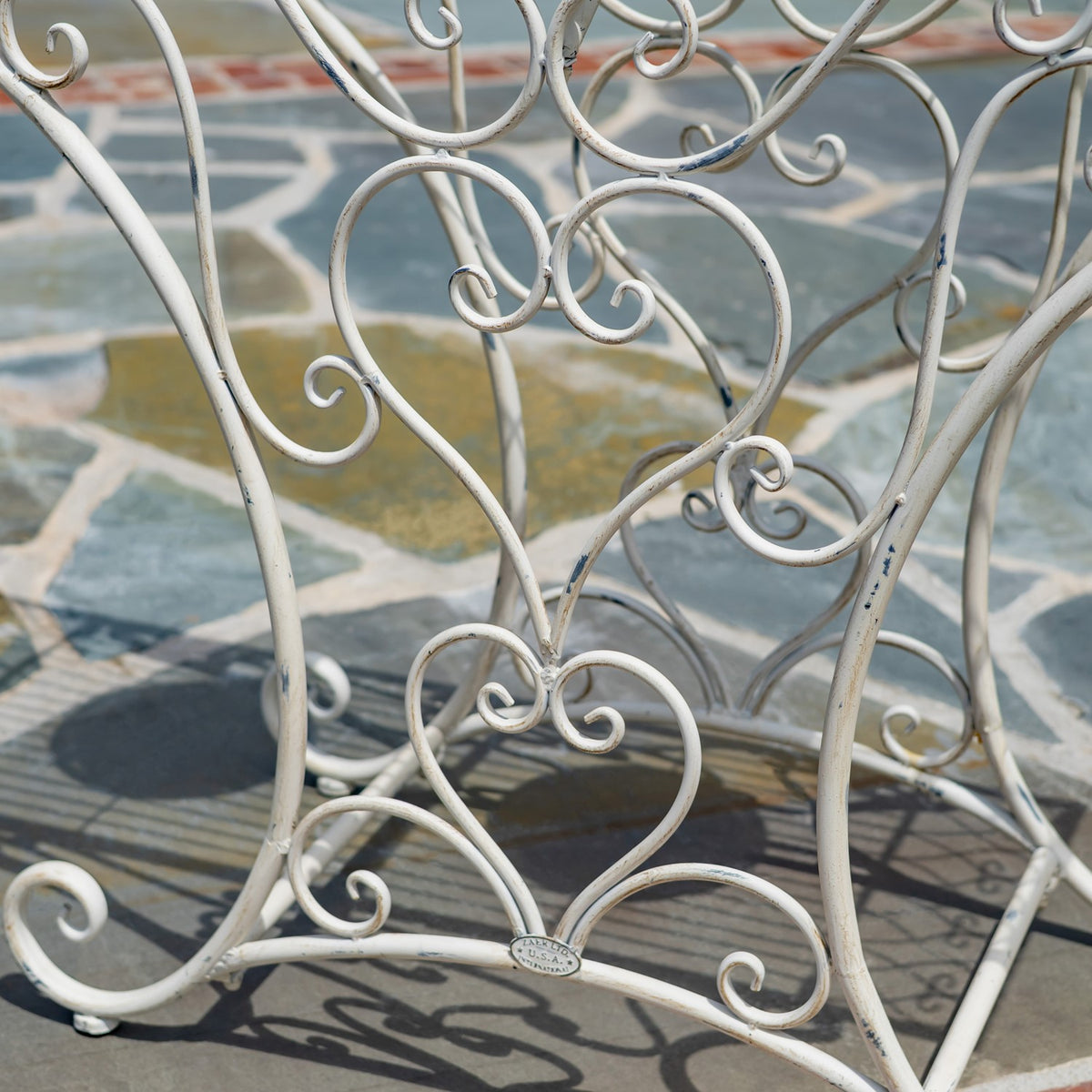 Close-up of curved white iron legs and scrollwork beneath the mosaic tabletop.