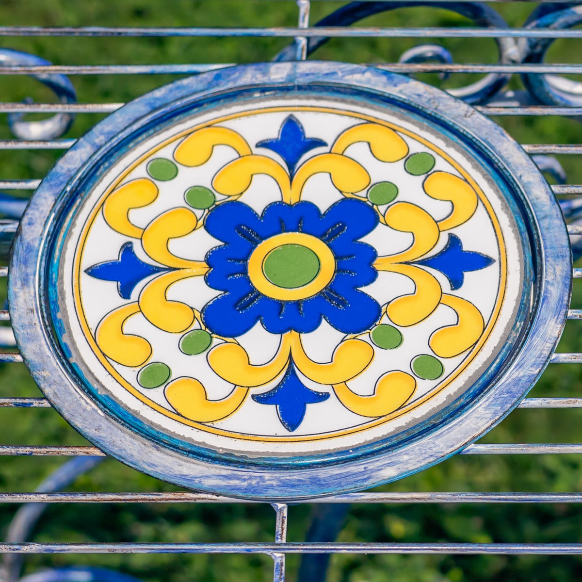 Close-up of a round mosaic tabletop with blue, yellow, and green floral patterns in a weathered blue frame.