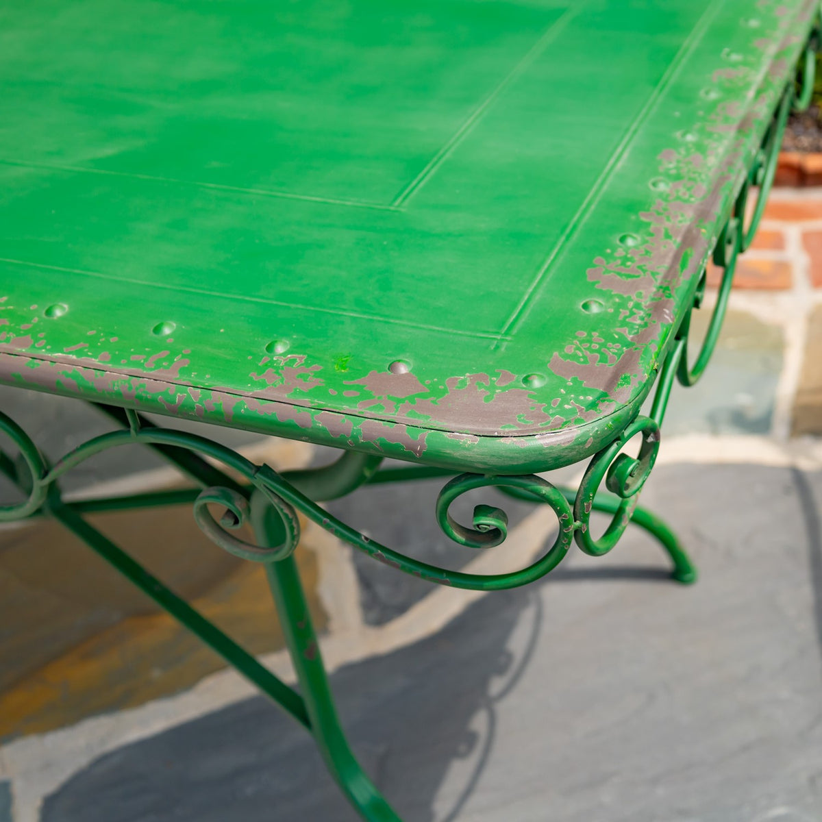 Close-up of a green metal tabletop with worn edges and curled scrollwork beneath.