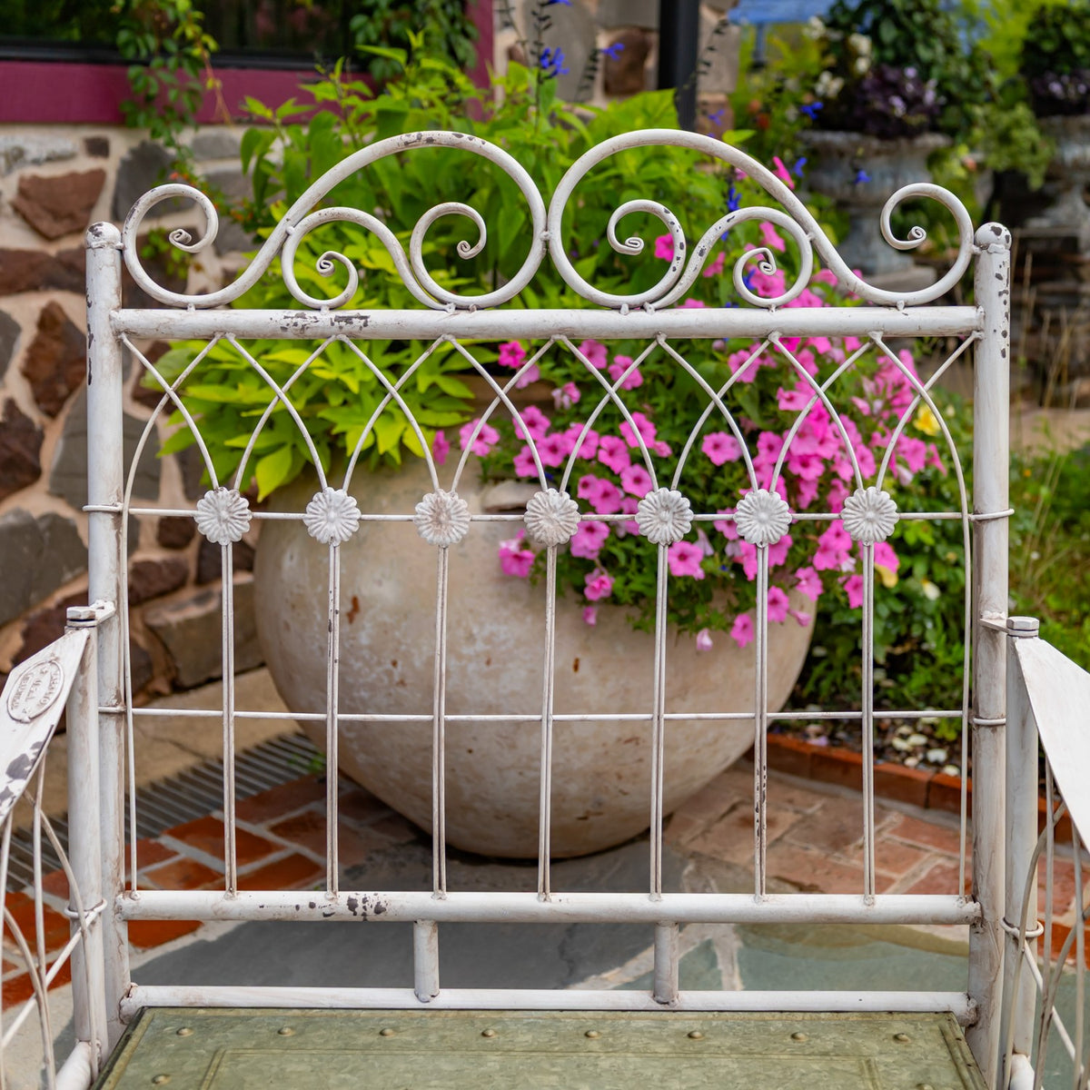 Close view of the chair’s curled metal backrest, flower-shaped accents and weathered white finish.