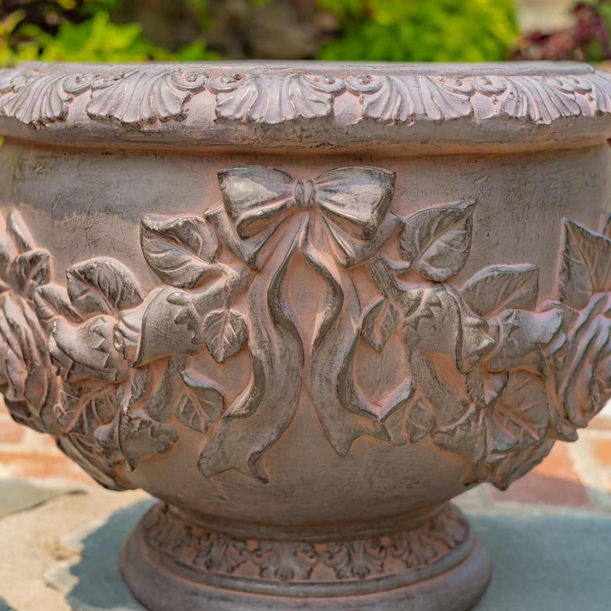 Close-up of a round planter with raised bow and floral details in a weathered rust finish.