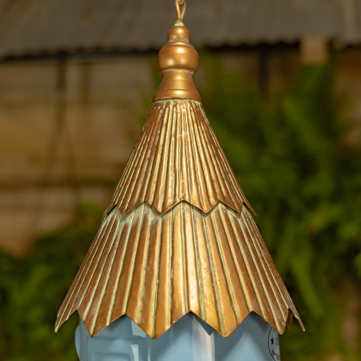 Close-up of the hanging birdhouse’s ribbed bronze-tone roof above its soft blue body.