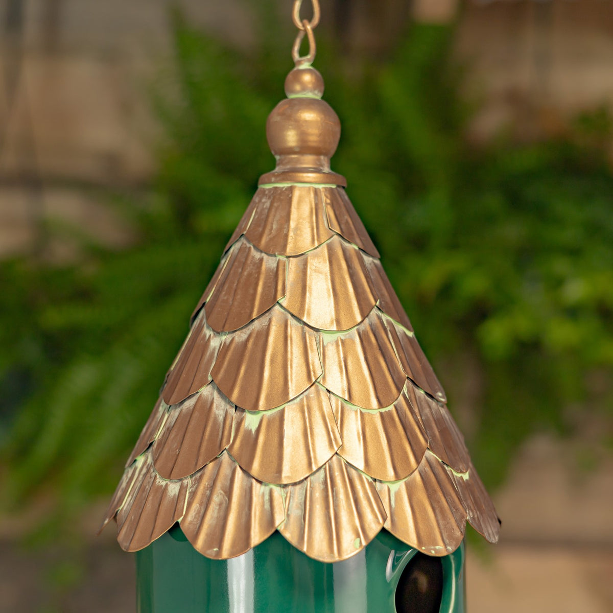 Close-up of the birdhouse’s layered copper-toned roof and dark round entrance against greenery.