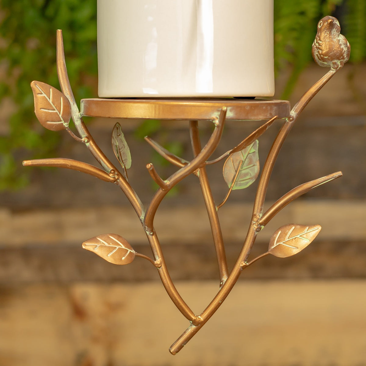 Bronze-tone branch-shaped base with metal leaves and a small bird ornament beneath a white cylinder.