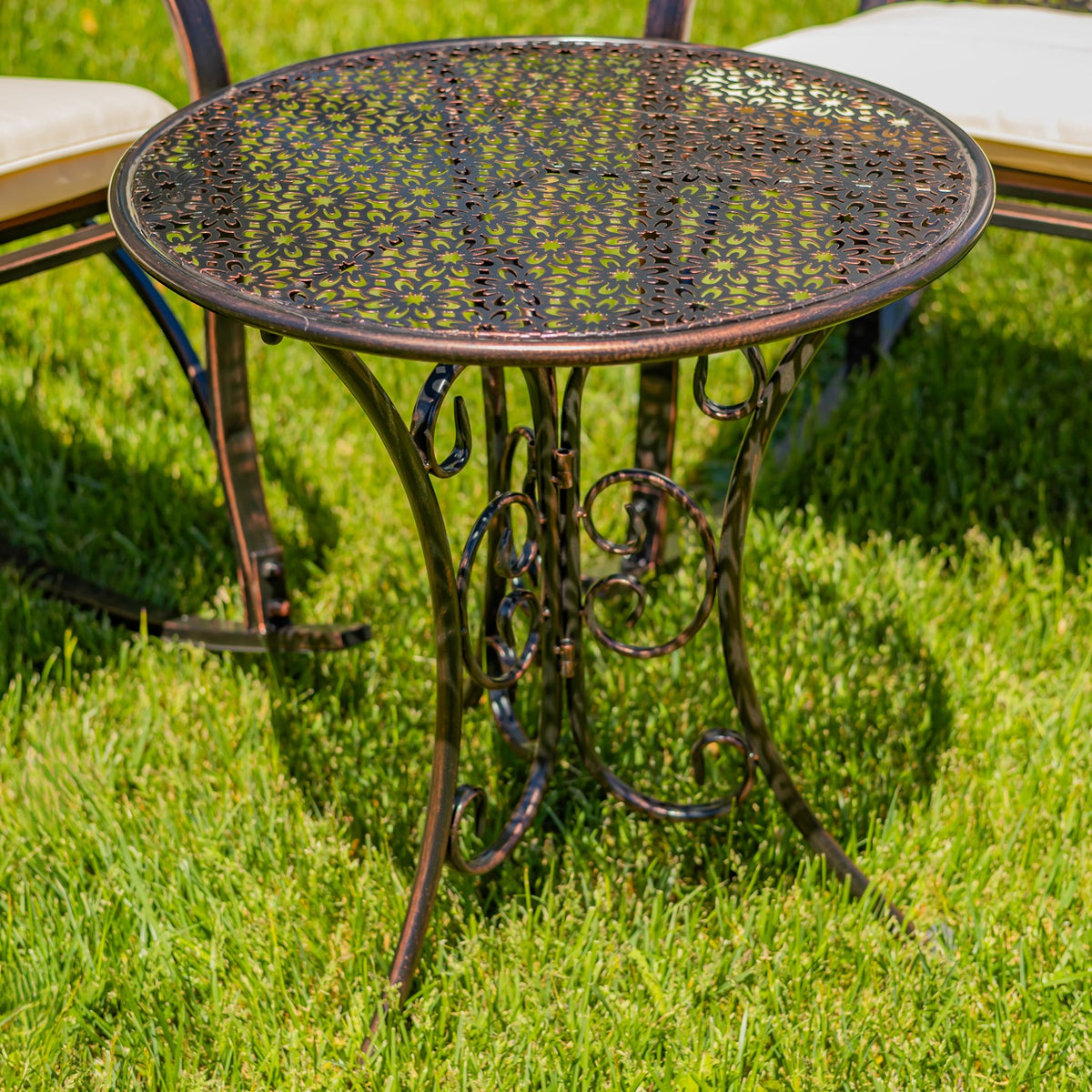 Round metal side table with a perforated floral top and curled decorative legs on a lawn.