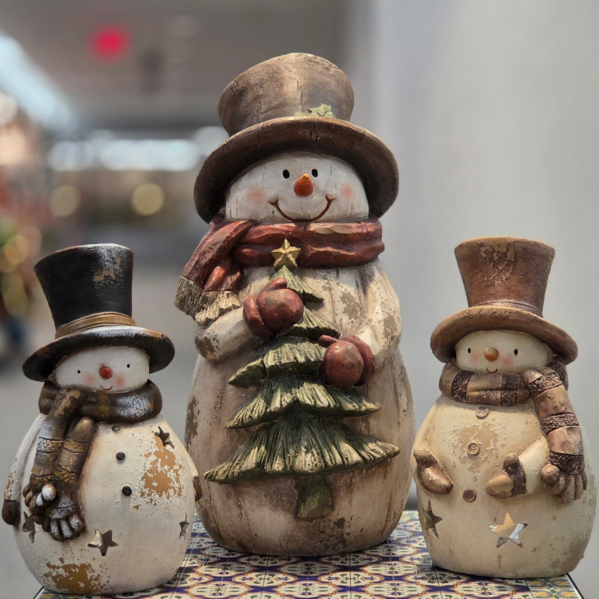 Tall snowman figurine holding a tree between two smaller snowmen on a table