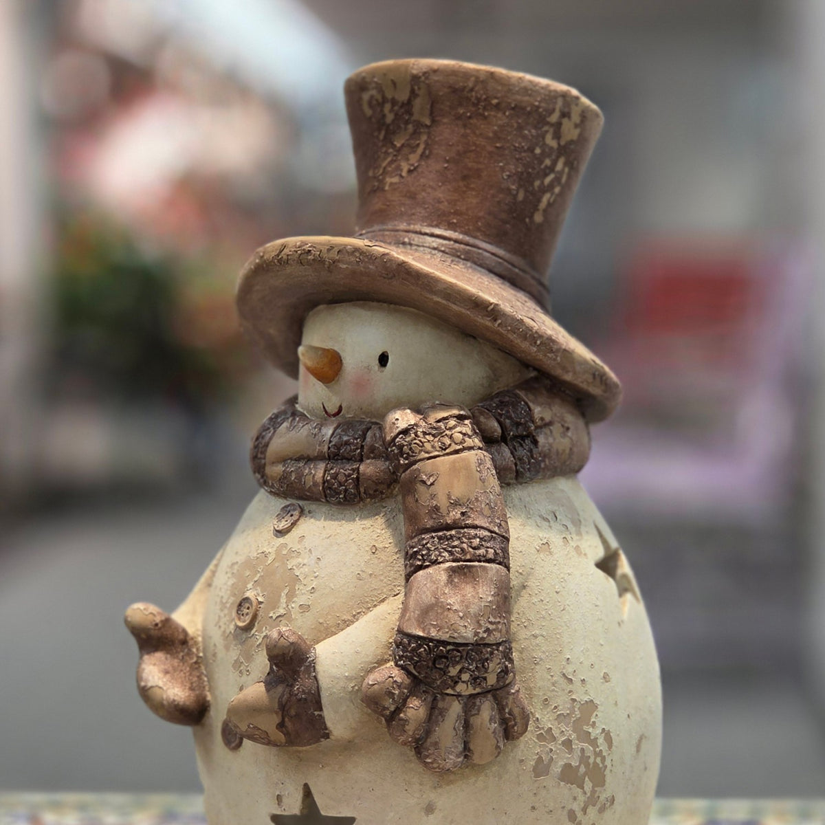Close view of a cream-colored snowman candleholder wearing a distressed brown top hat and scarf.
