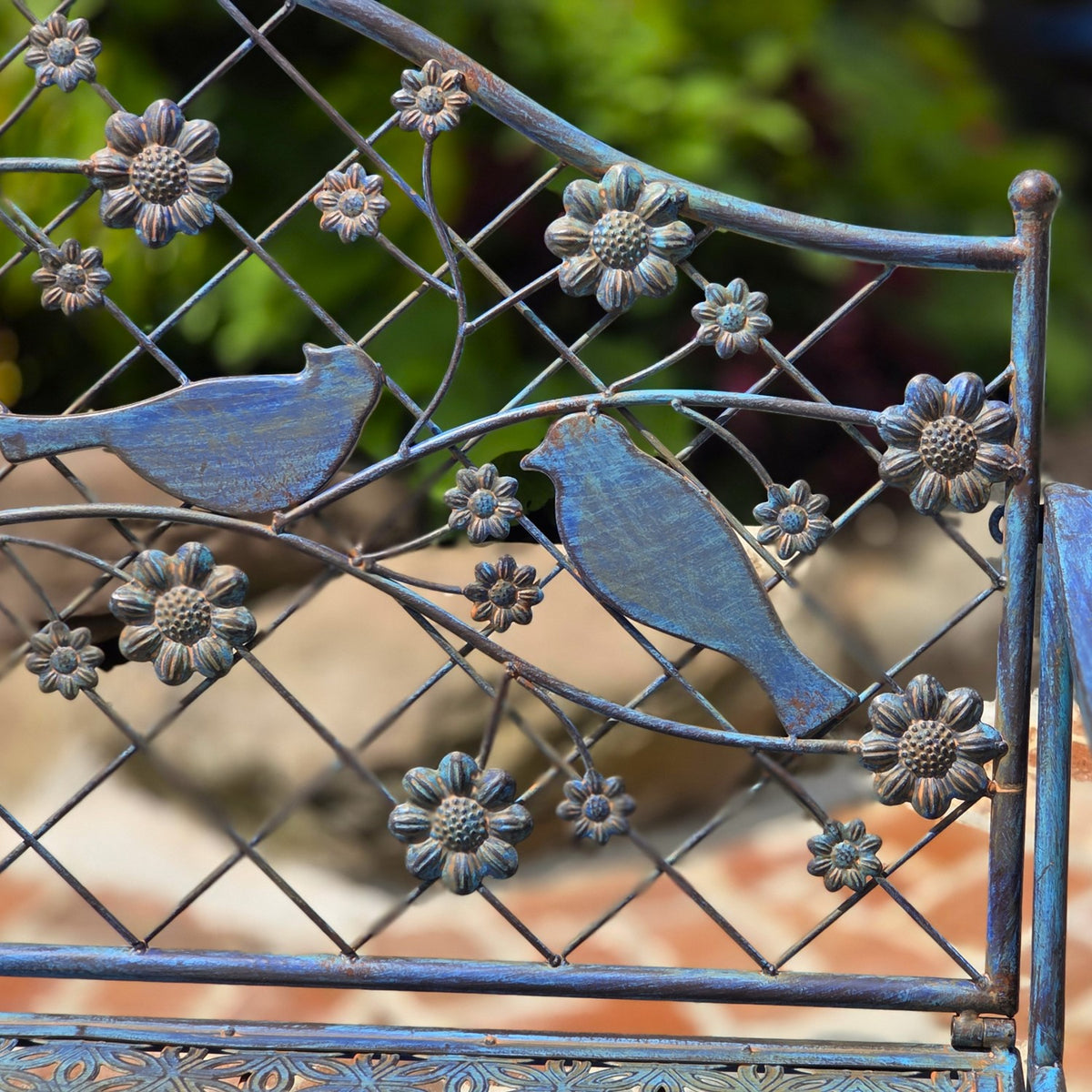 Metal backrest detail with two bird silhouettes, flower-shaped ornaments, and a crisscross wire pattern.