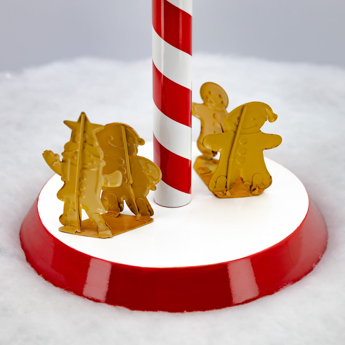 Close-up of gingerbread figures around the striped candy cane post on a red-and-white base.
