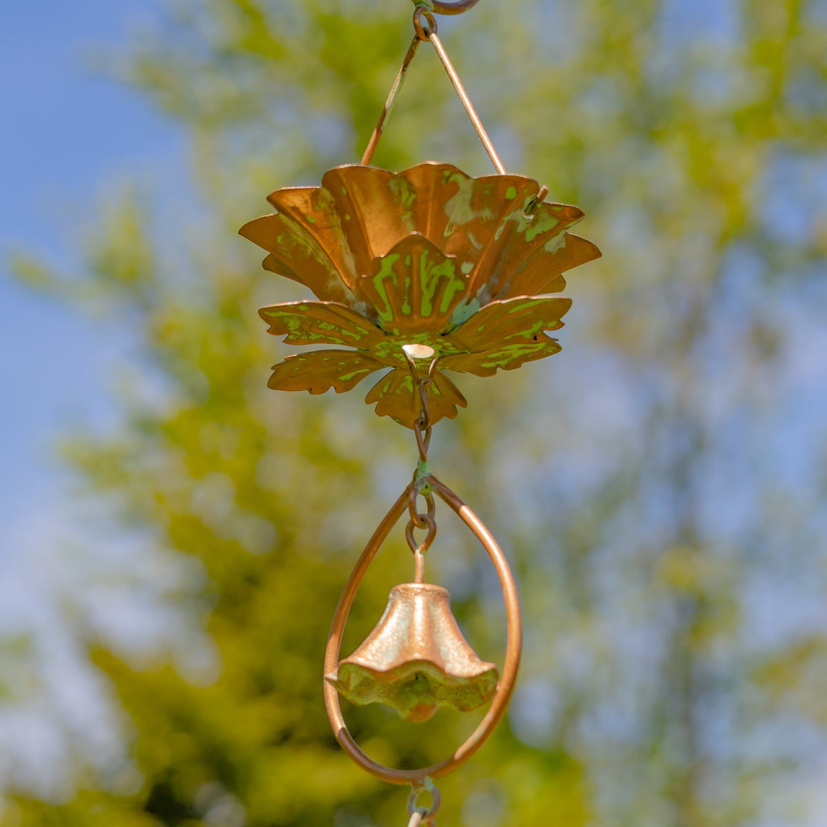 Close-up of a copper-toned lotus-shaped rain chain cup above a bell in an oval frame.