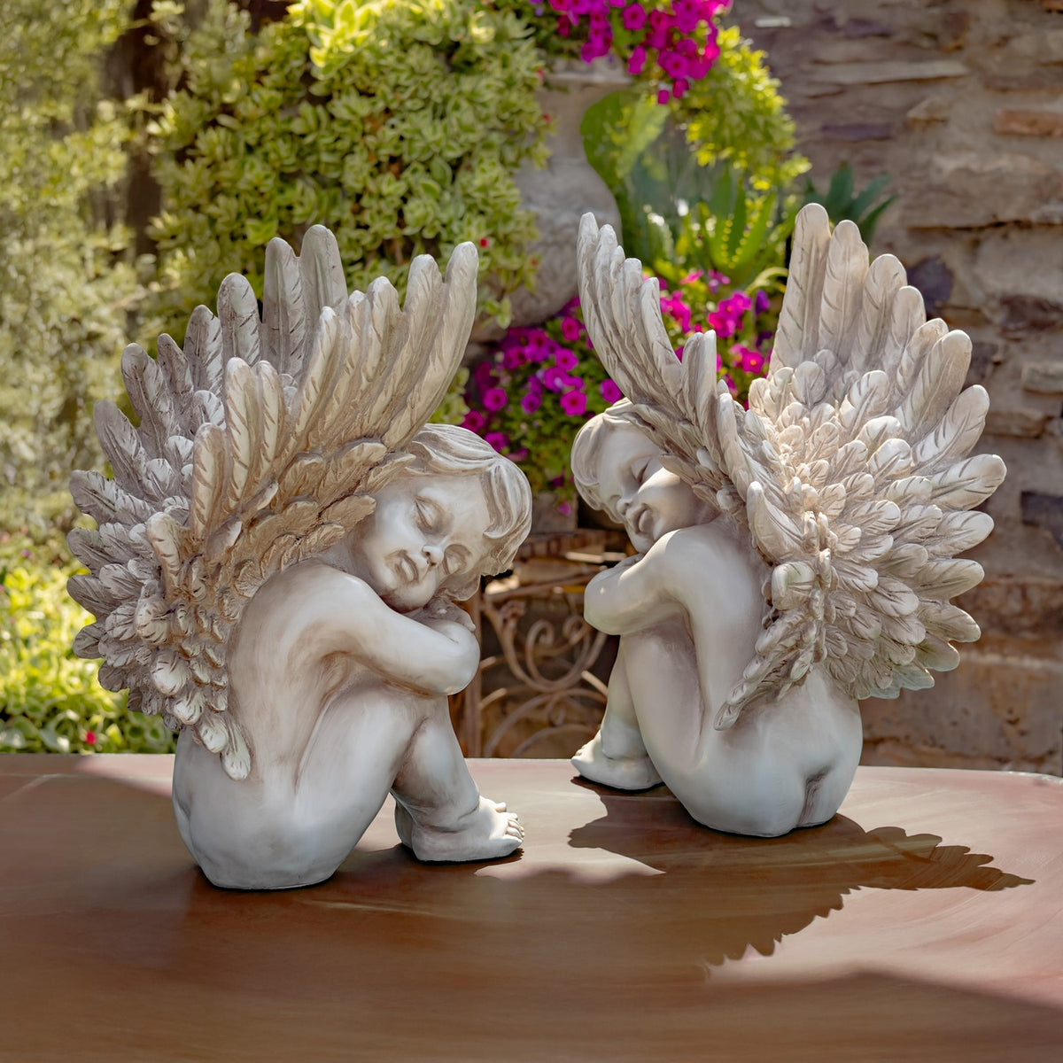 Two antique grey cherub statues viewed from behind on an outdoor table