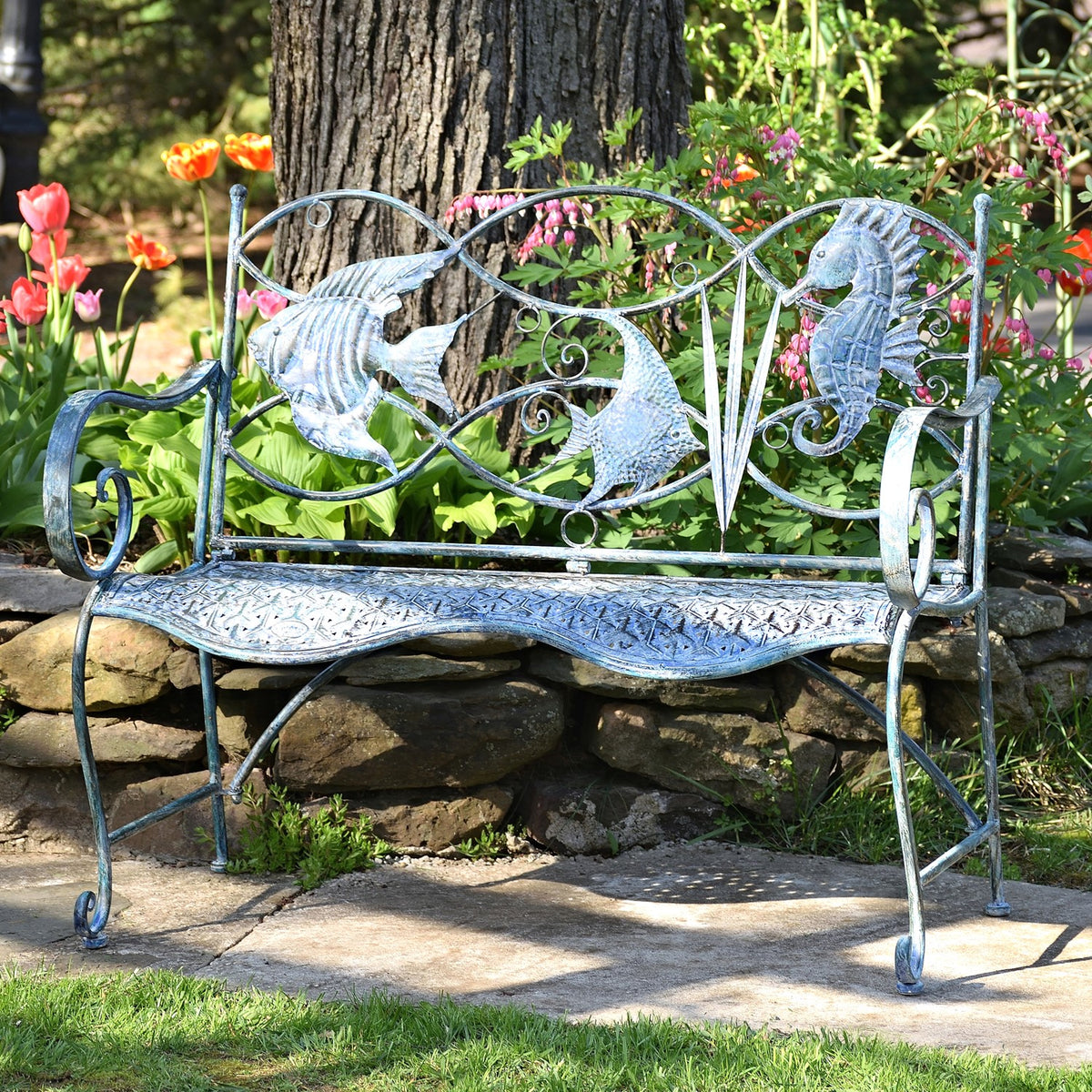 Coastal blue iron garden bench displayed among flowers beside a stone wall