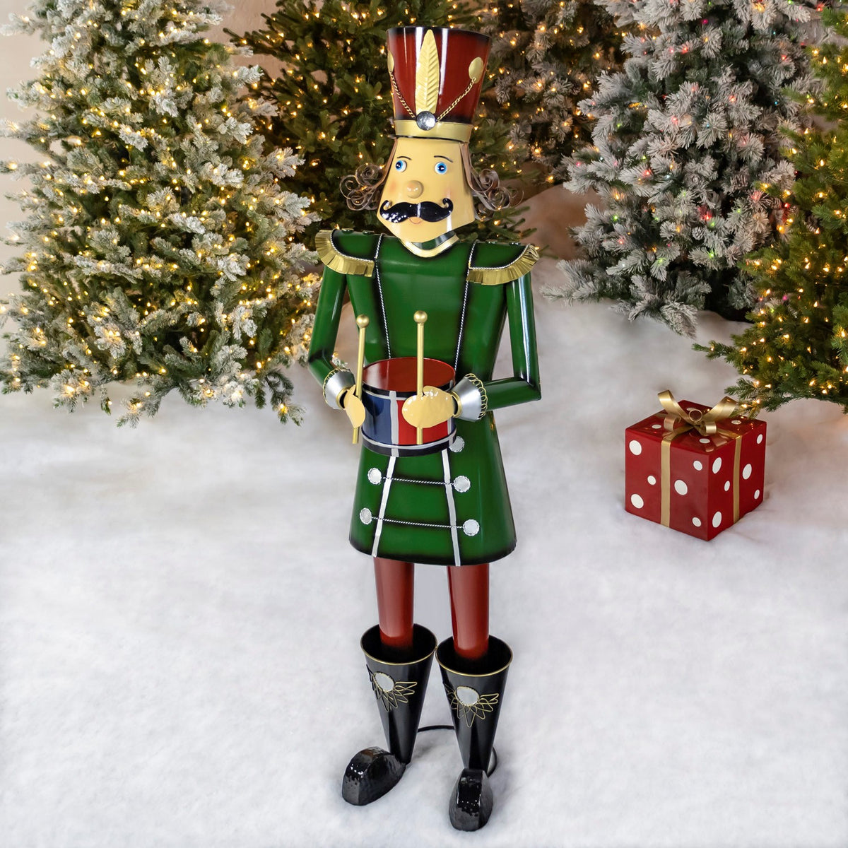 Full green nutcracker holding a drum beside a red present