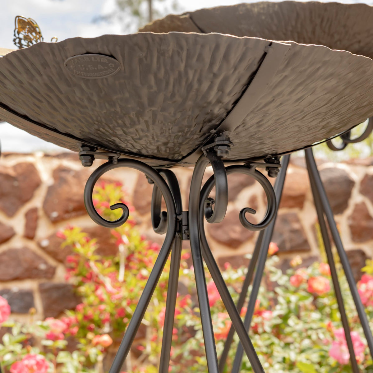 View beneath the textured birdbath bowl, showing its curled iron supports and slender legs.