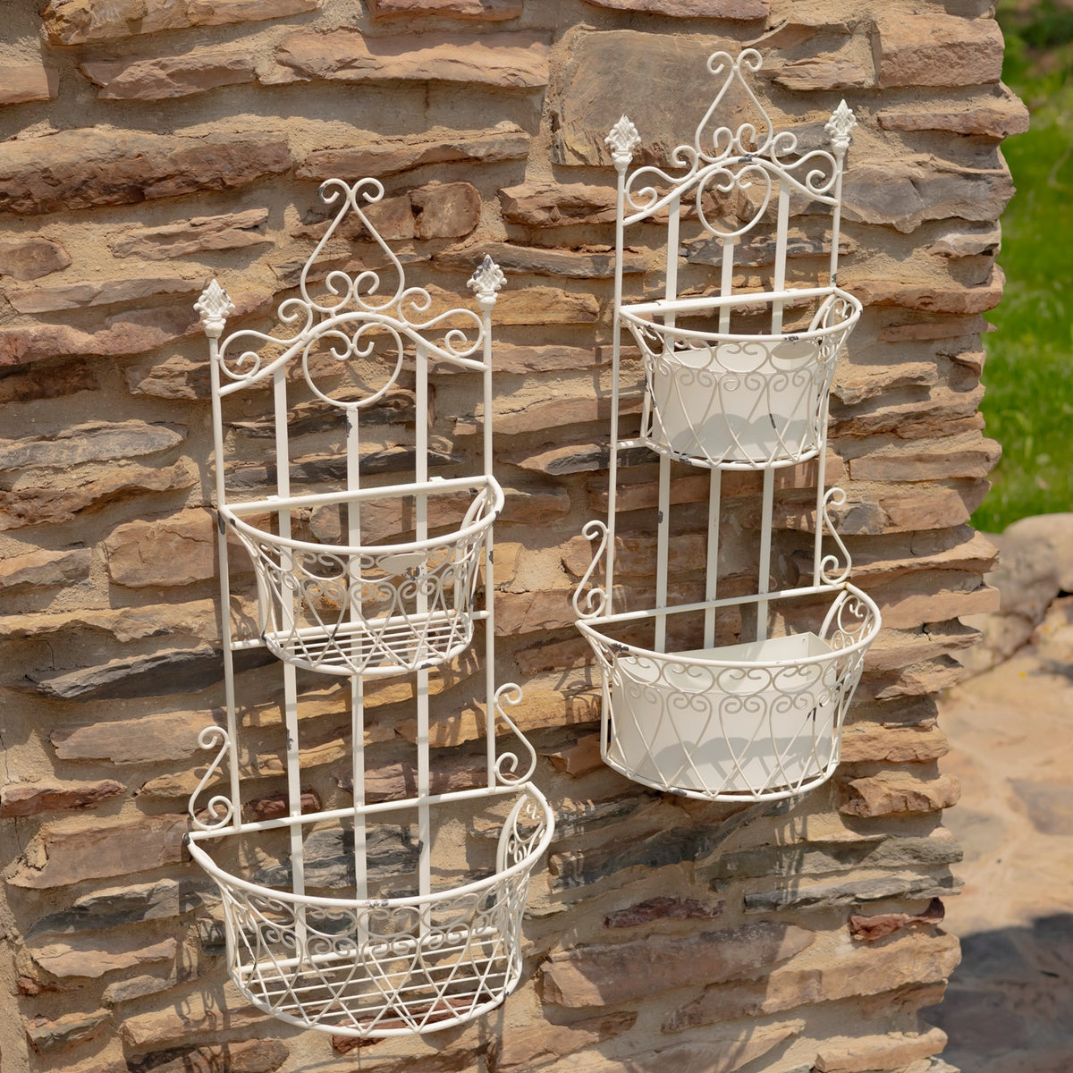 Two empty white wire wall planters with decorative scrollwork against a stone wall.