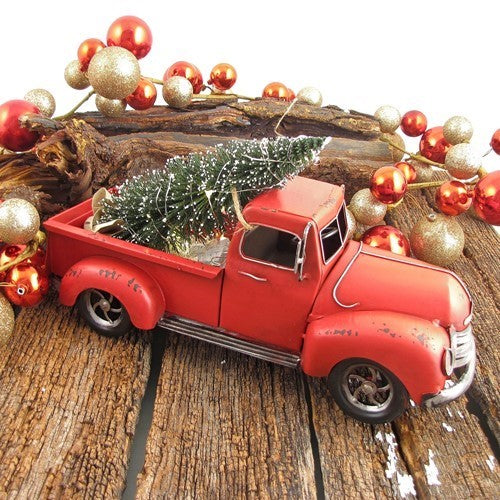 Angled view of a red pickup with a small tree in its bed, surrounded by ornaments on a wooden surface.