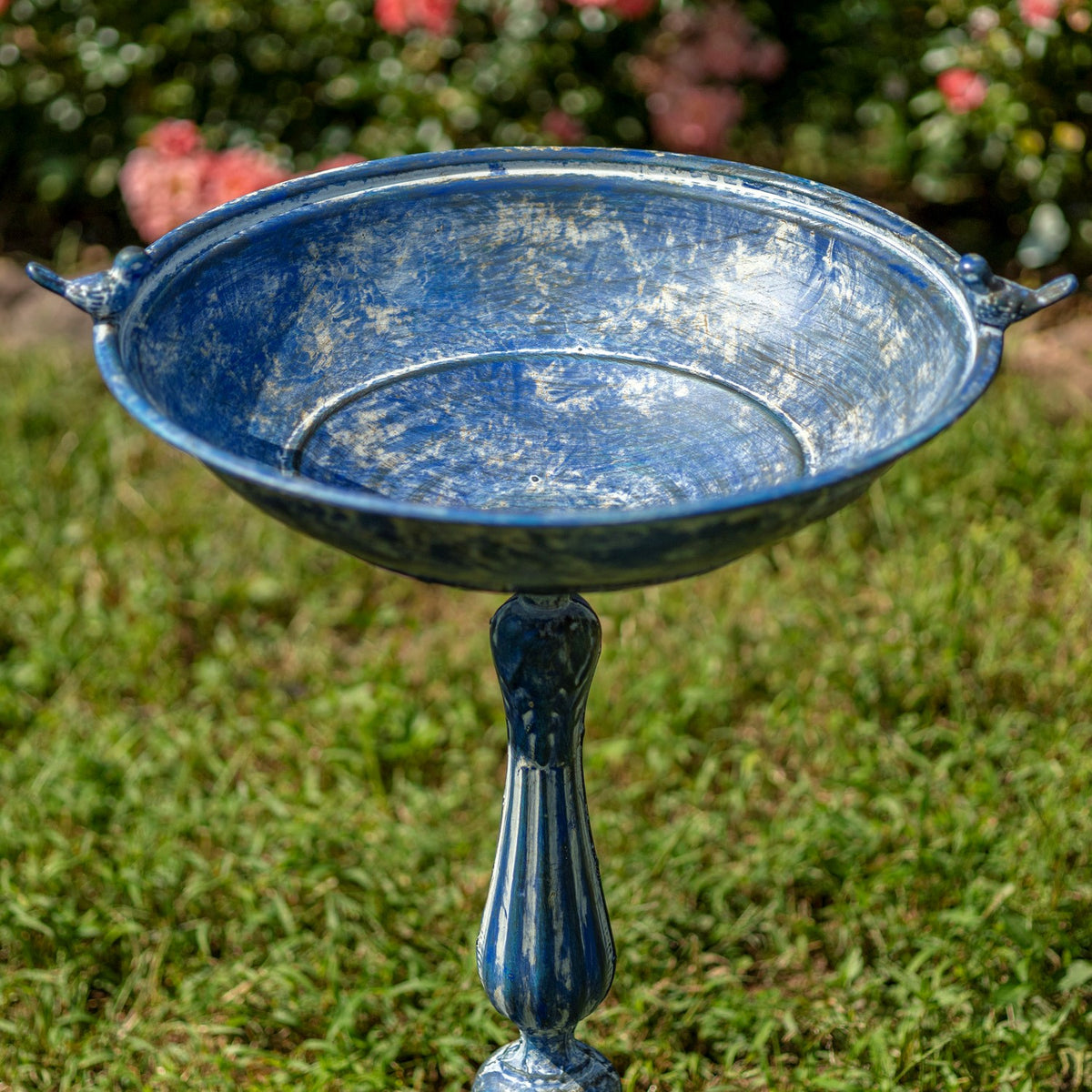 Close view of the birdbath’s shallow, weathered blue bowl and small bird ornaments on its rim.