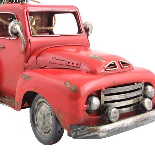 Close-up of the pickup’s weathered red hood, grille, round headlights, windshield and front wheel against white.