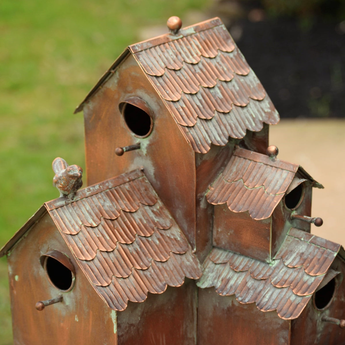 Close-up of the antique copper birdhouse stake's layered roofs and entry holes