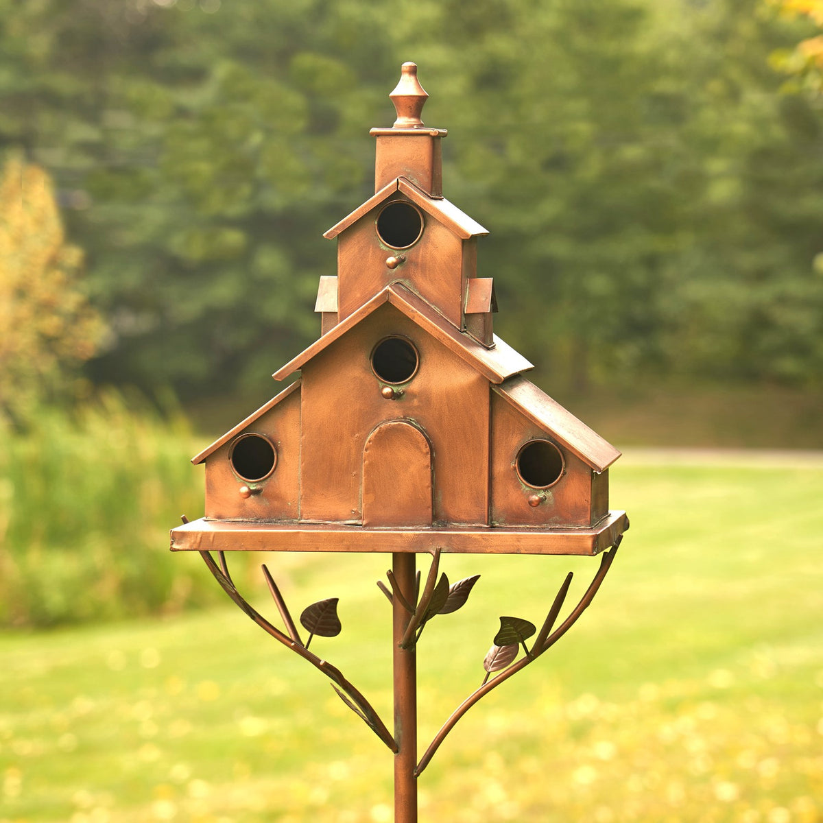 Front of a multi-roof birdhouse with round openings and leaf details on its stake.