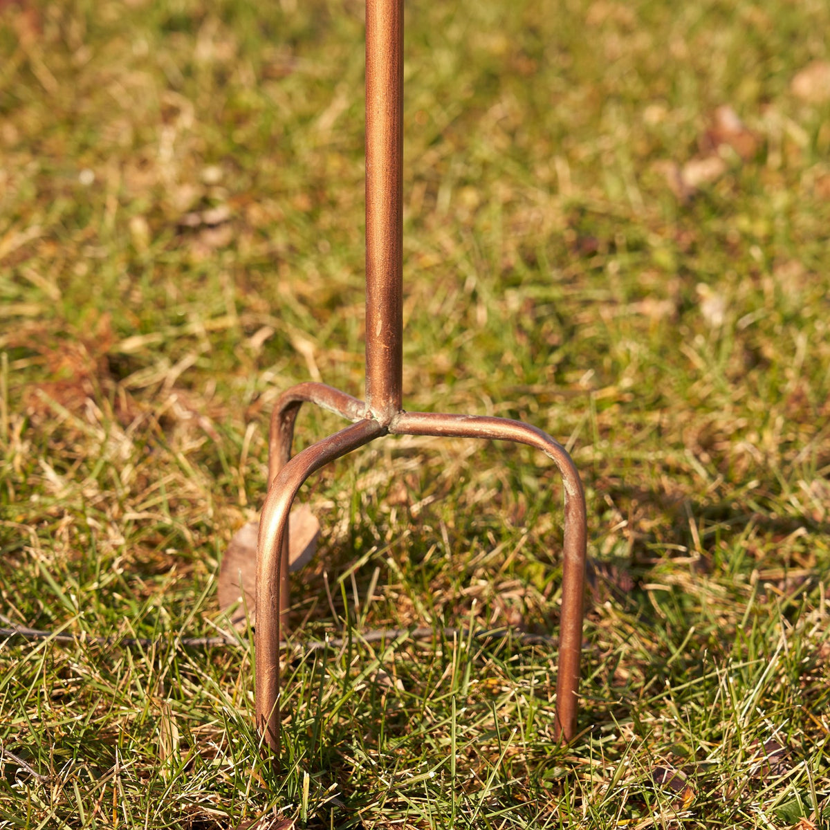 Close-up of the three-prong copper garden stake base in grass