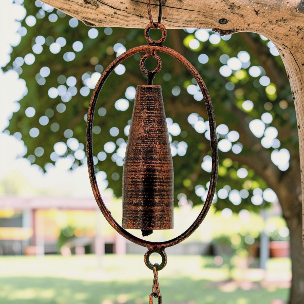 A textured bronze-toned cylinder hangs inside an oval metal frame beneath a branch.