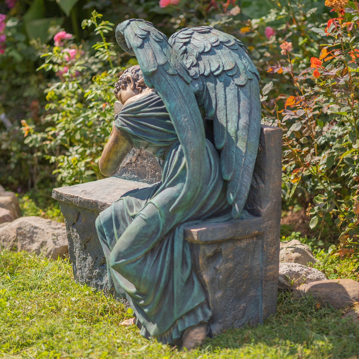 The seated angel is viewed from behind, showing her layered wings and draped gown on the bench.