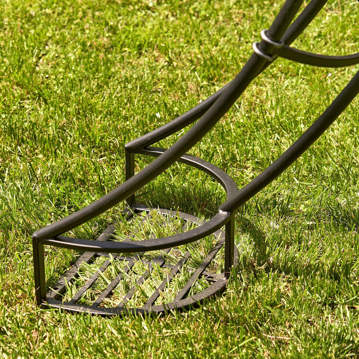 Close-up of the black iron arch's slatted plant stand base on grass