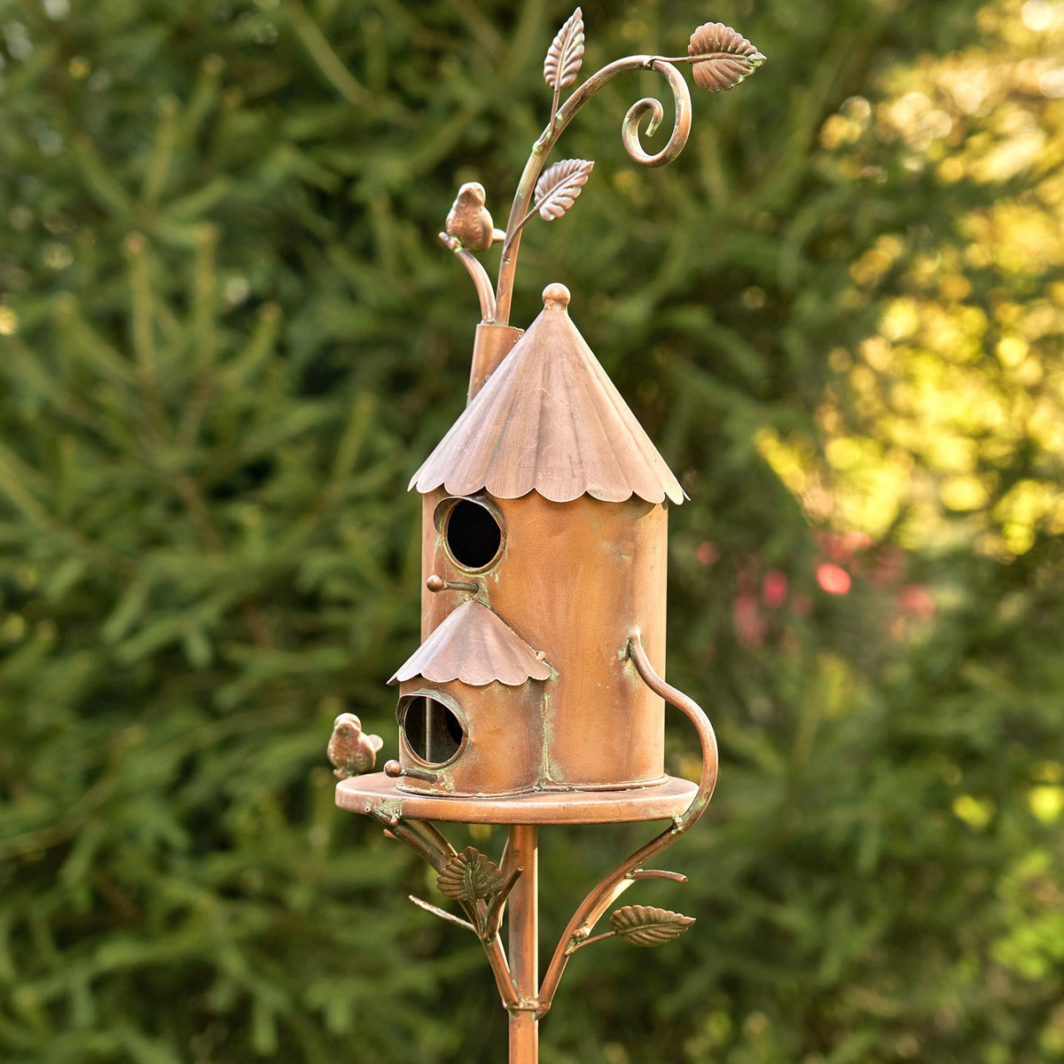 Antique copper two-story birdhouse shown from an angled side view in a garden