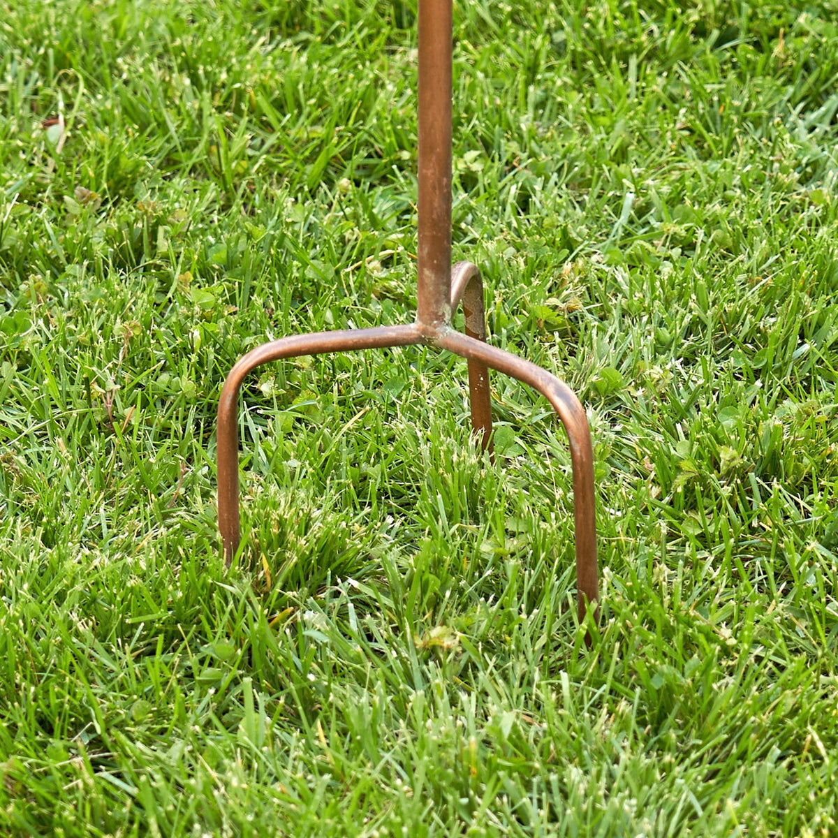Three-pronged copper-tone stake base standing in grass