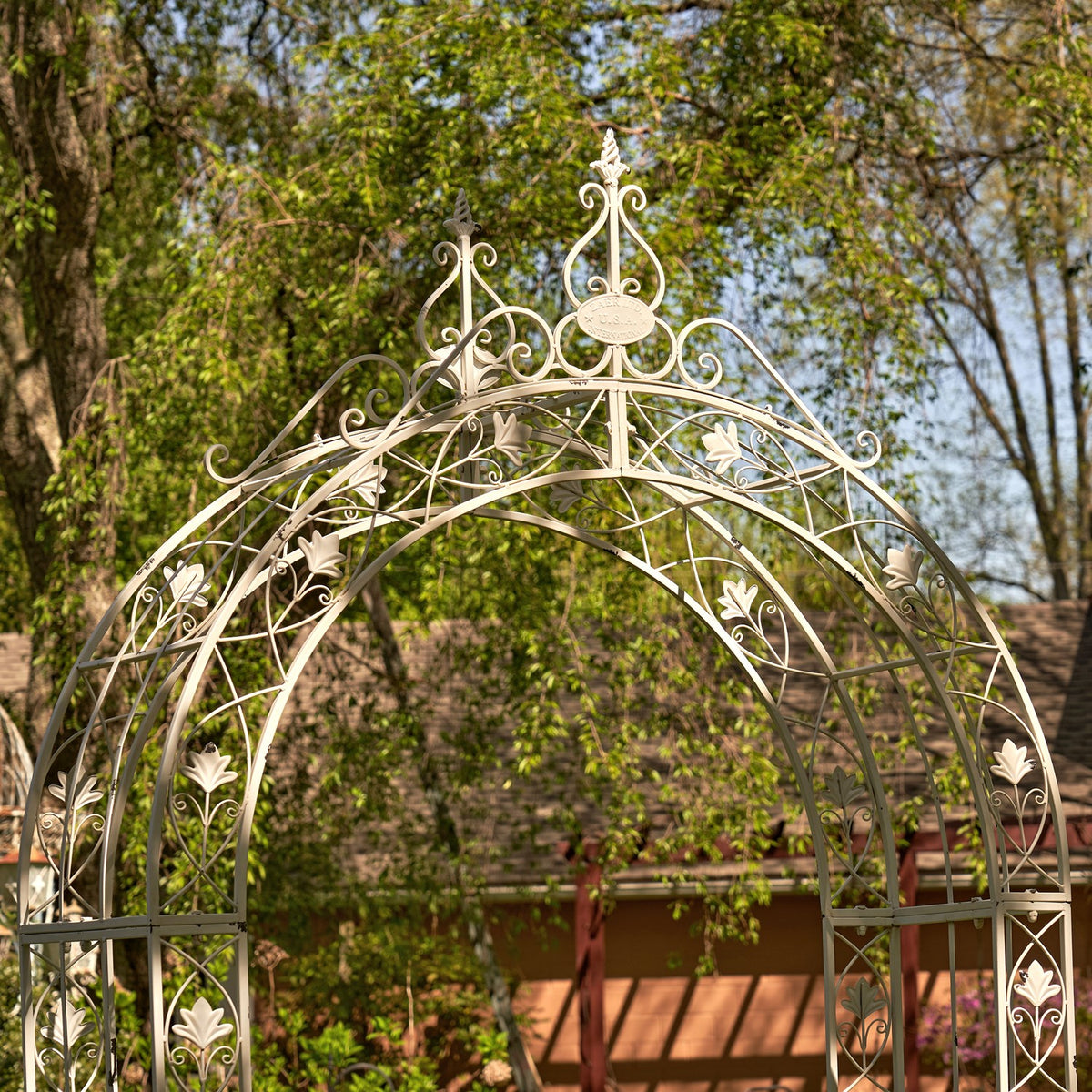 Ornate crest and curved floral metalwork on the pale garden arch.