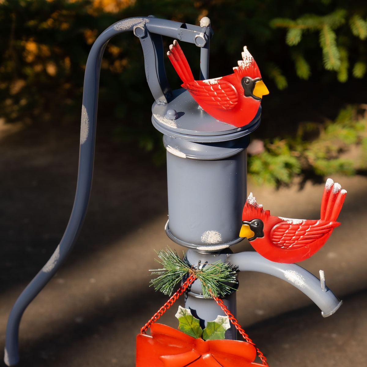 Closer view of the pump handle, two red cardinals, greenery, and the top of the hanging sign.