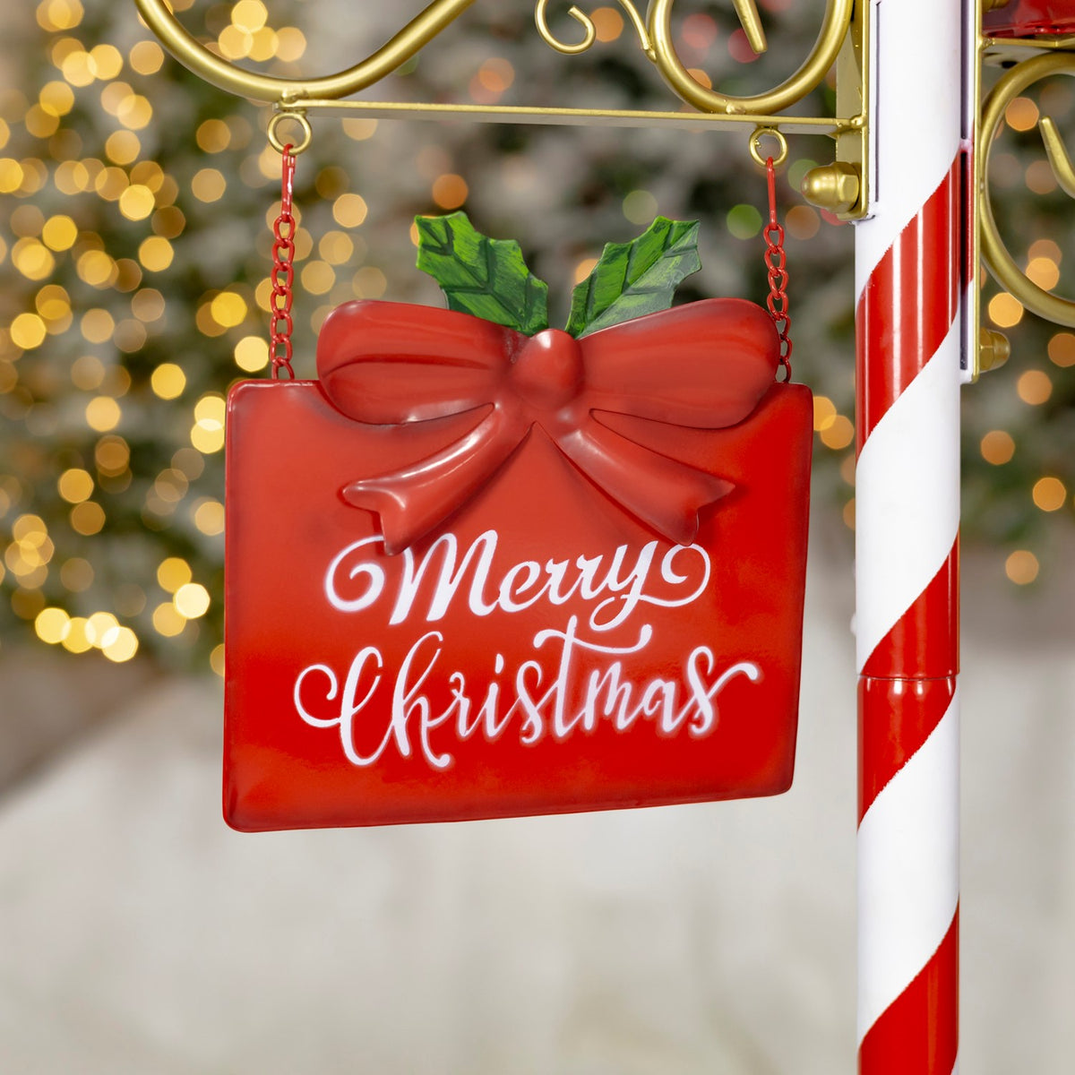 Red hanging sign with a raised bow and holly leaves, suspended by red chains beside the striped post.