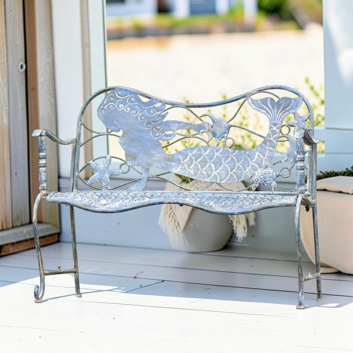 Full view of a metal bench with mermaid and sea-life cutouts, displayed on a bright porch.