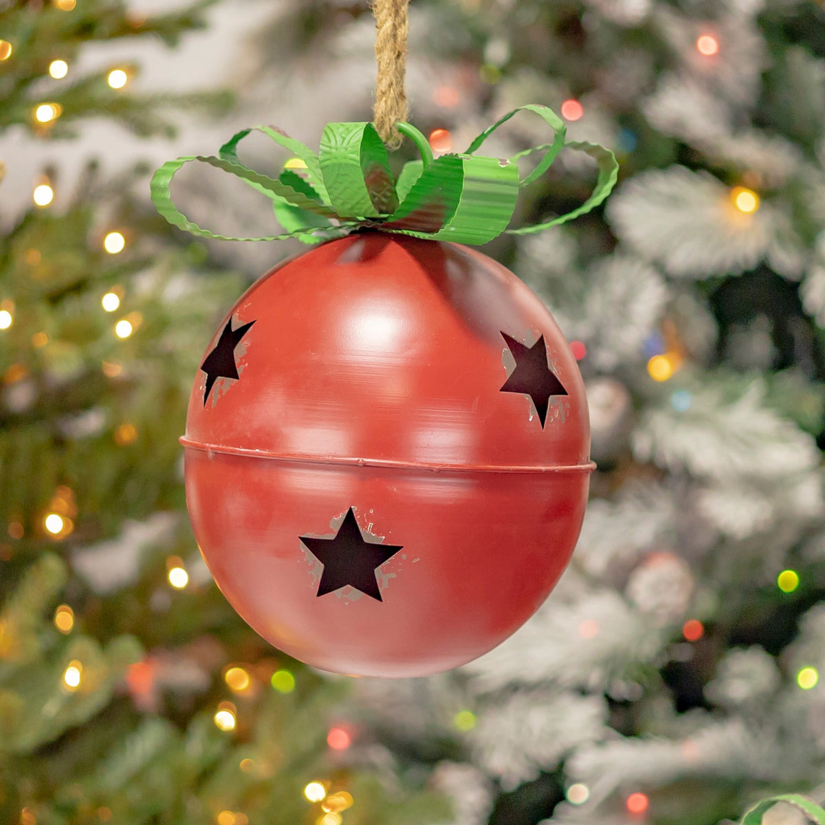 Red hanging bell with star cutouts and a green bow against holiday lights