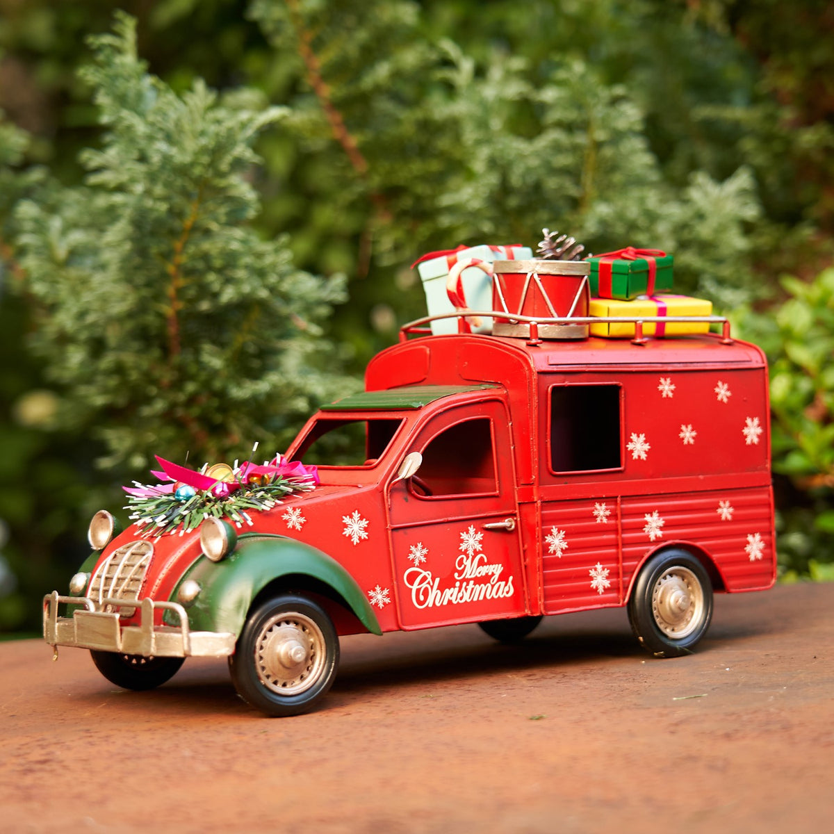 Red holiday truck decorated with white snowflakes and greenery across its hood, with presents on top.