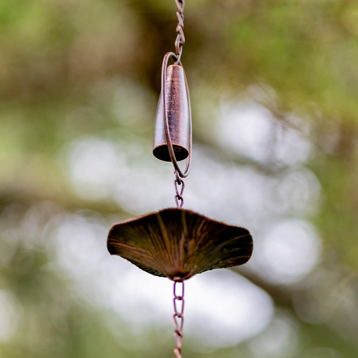 Close-up of a bronze chime and the underside of a flared mushroom-shaped rain chain cup.