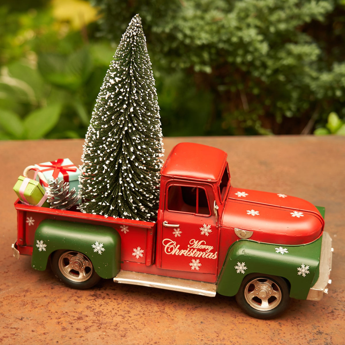 High side view of a red and green Christmas truck carrying a miniature tree and gifts