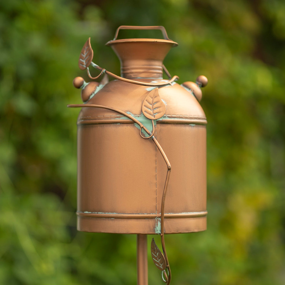 Back of the copper-toned milk-can birdhouse, showing its raised leaf-and-vine decoration and support stake.