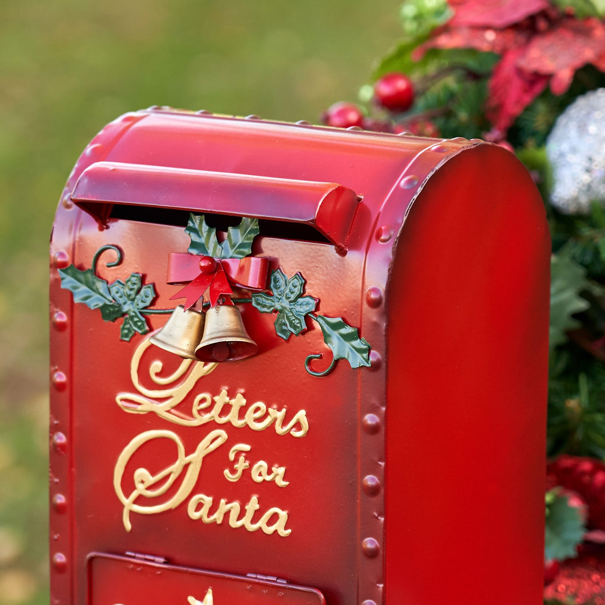 Angled view of the red mailbox showing its curved side, mail slot, bells, and holly trim.