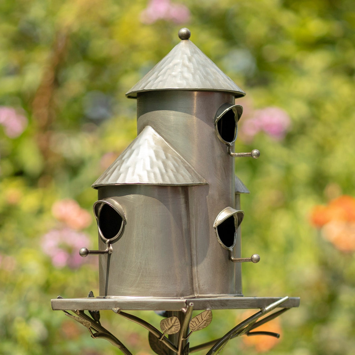 Angled view of the silver triple birdhouse, showing entry holes on its cylindrical houses and leaf-shaped stand.