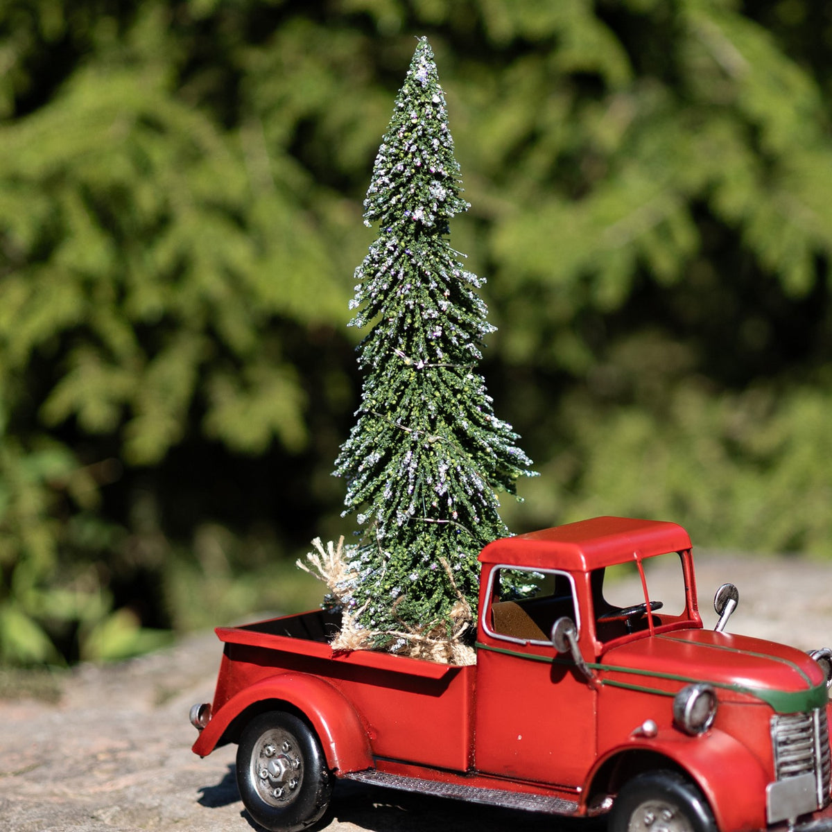 Red vintage-style pickup truck with a tall snow-dusted Christmas tree in its open bed.