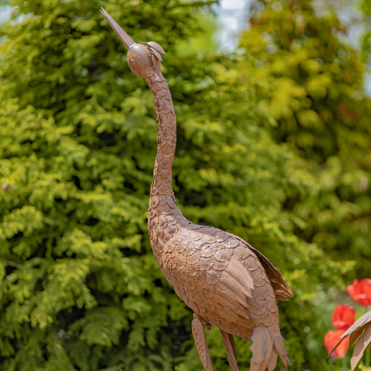 Single tall rust-colored crane sculpture shown from the side in a garden