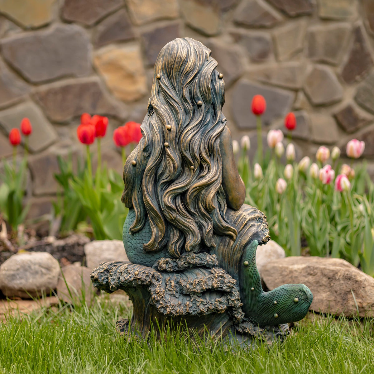 Back view of the seated mermaid statue, showing its long wavy hair and curled tail beside the rock.