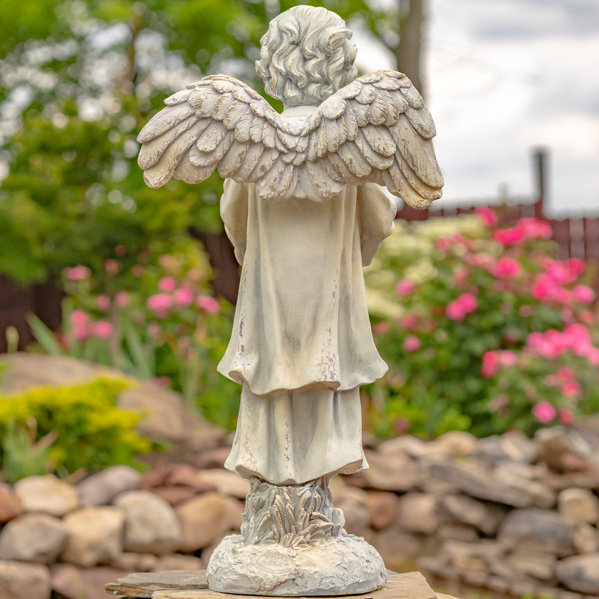 Back view of the angel statue showing its layered wings, robe and textured base.