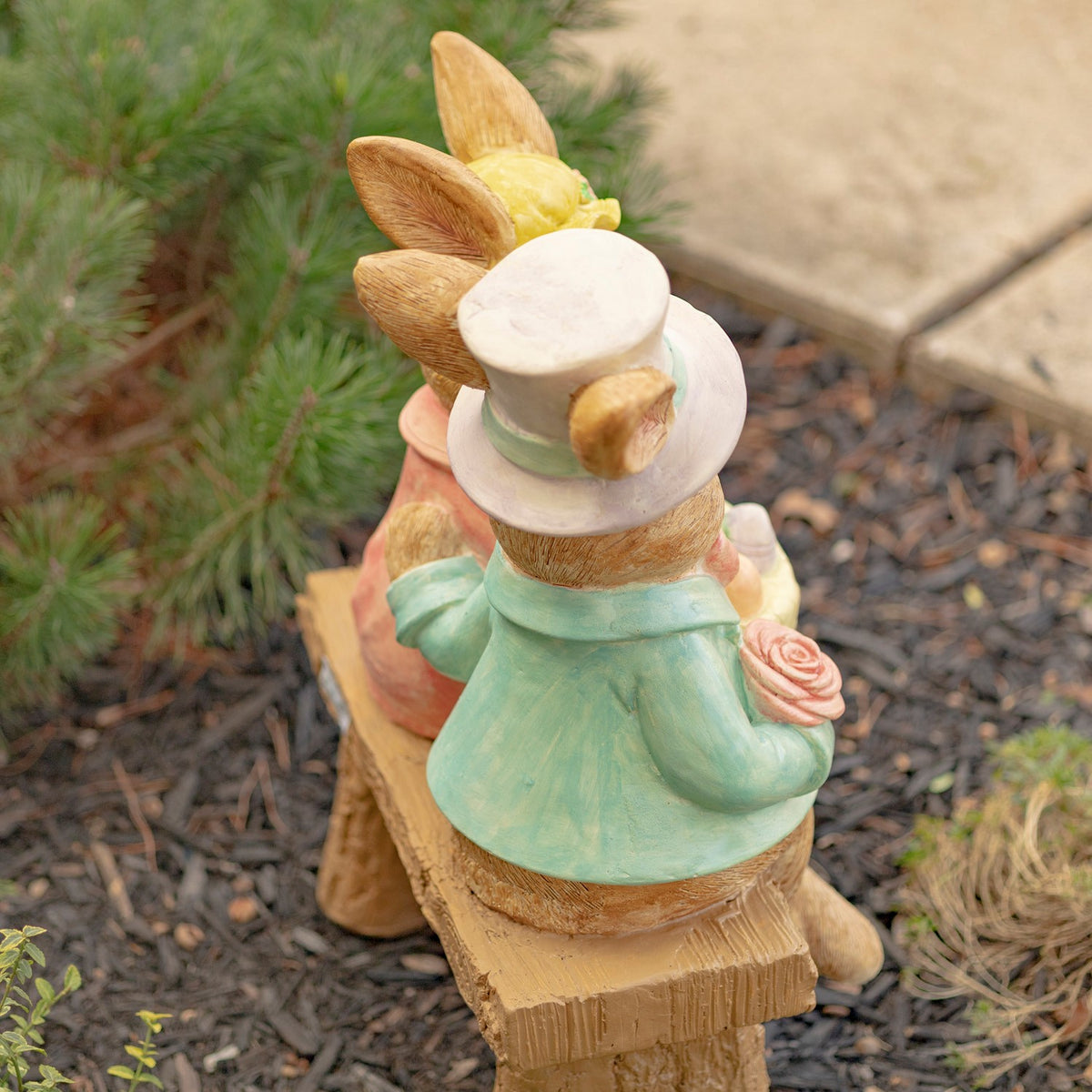 View from behind of the rabbit couple seated on a bench, showing their clothing and the bench seat.
