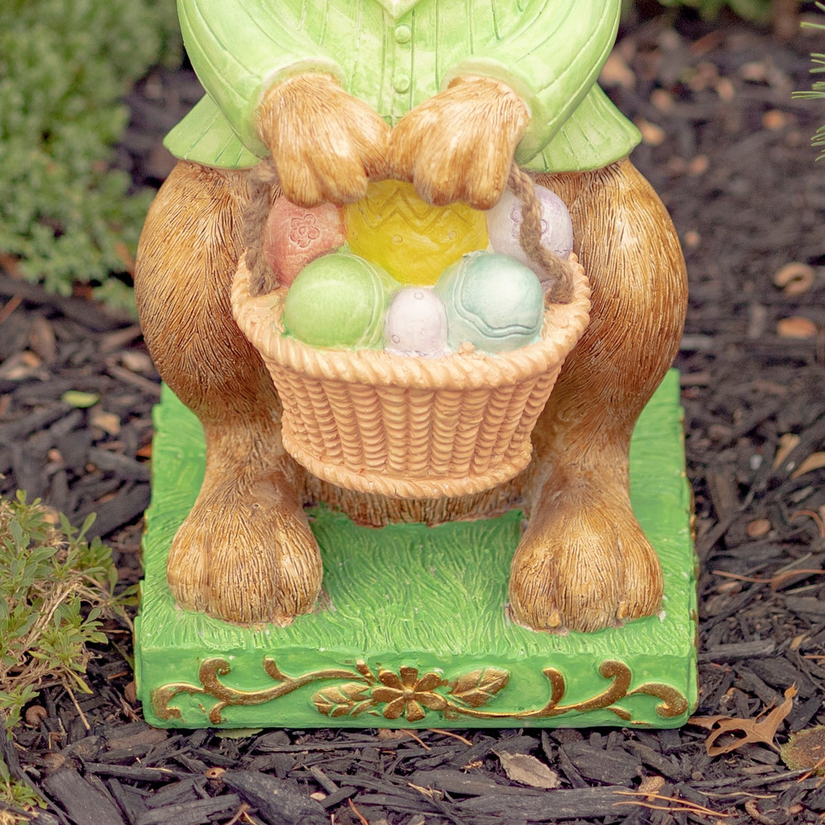 Close-up of the rabbit’s paws holding a woven basket filled with pastel eggs above a decorated green base.