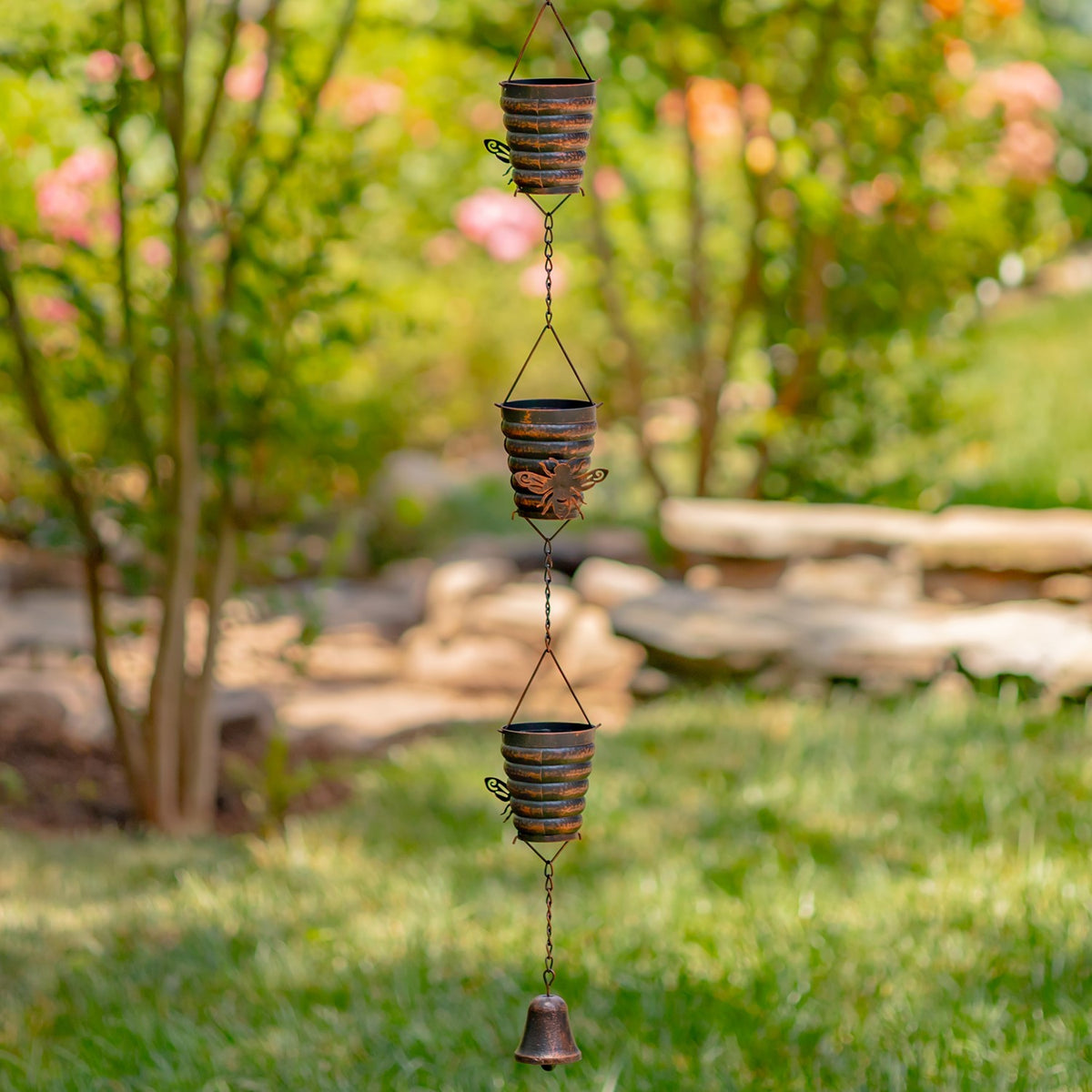 Antique bronze bucket hive rain chain hanging above grass in a garden