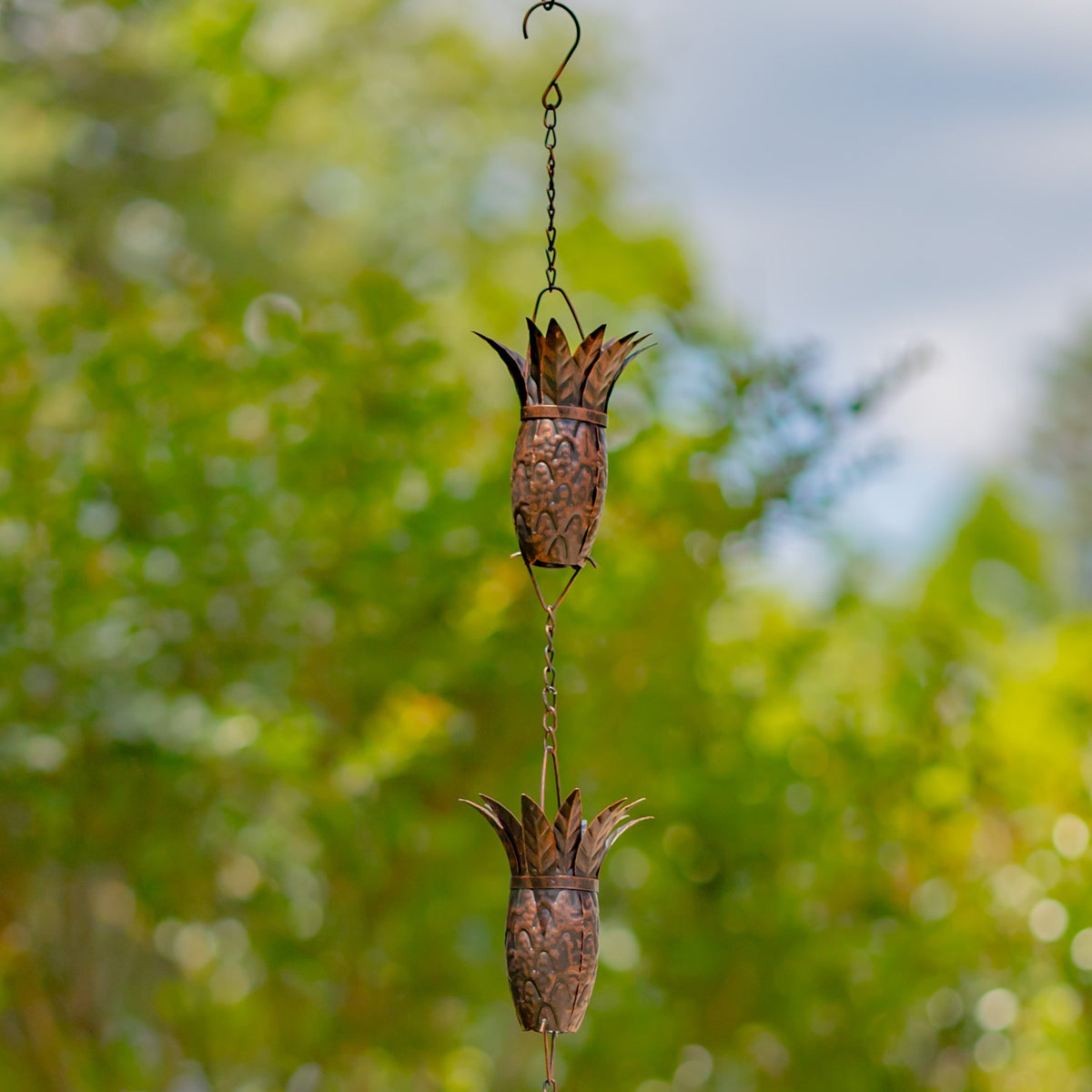 Antique bronze rain chain hanging from a hook with two pineapple-shaped links
